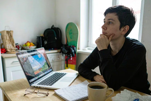 A rider planning a snowboard trip at a kitchen table with a laptop and notebook