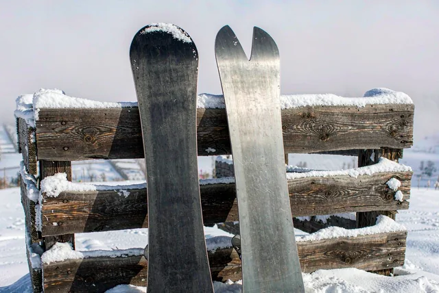 Two snowboards leaning side by side against a snow-covered wooden fence