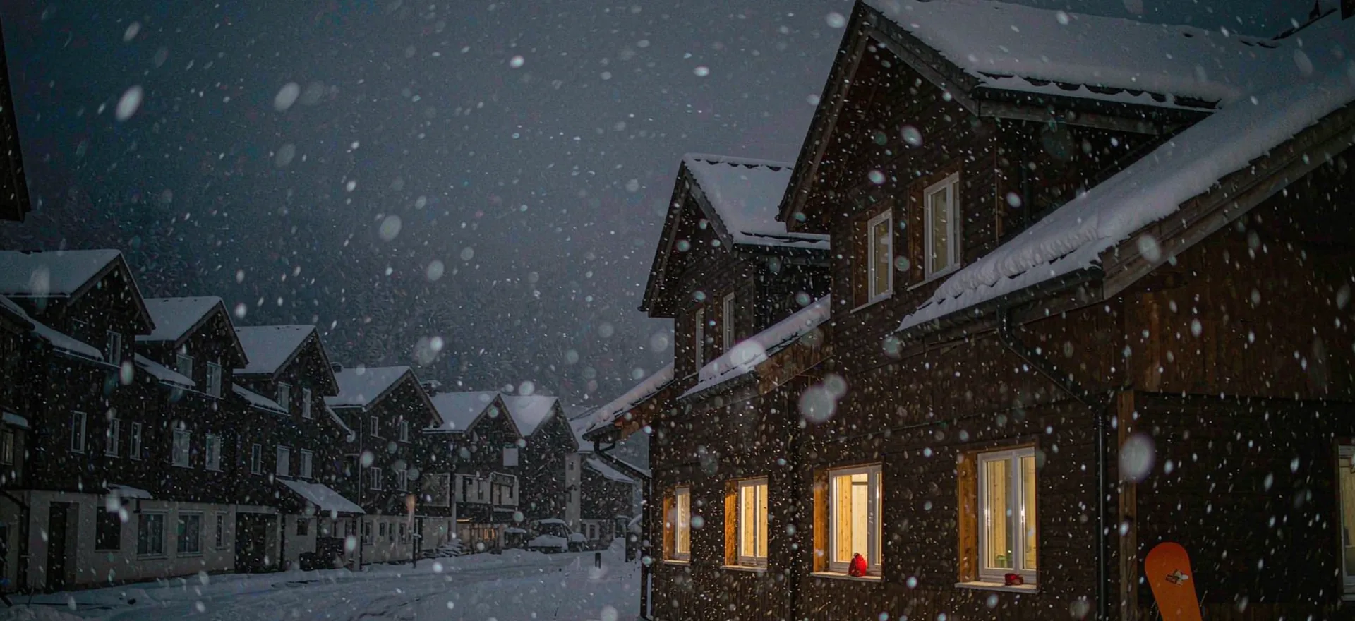 An alpine village at night with snow falling and warm window lights
