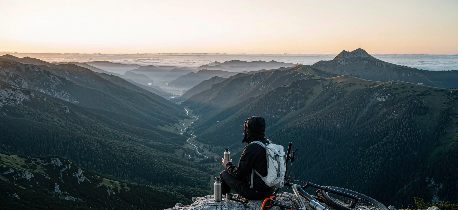 A snowboarder sitting on a summit at dawn looking out over a sea of alpine peaks