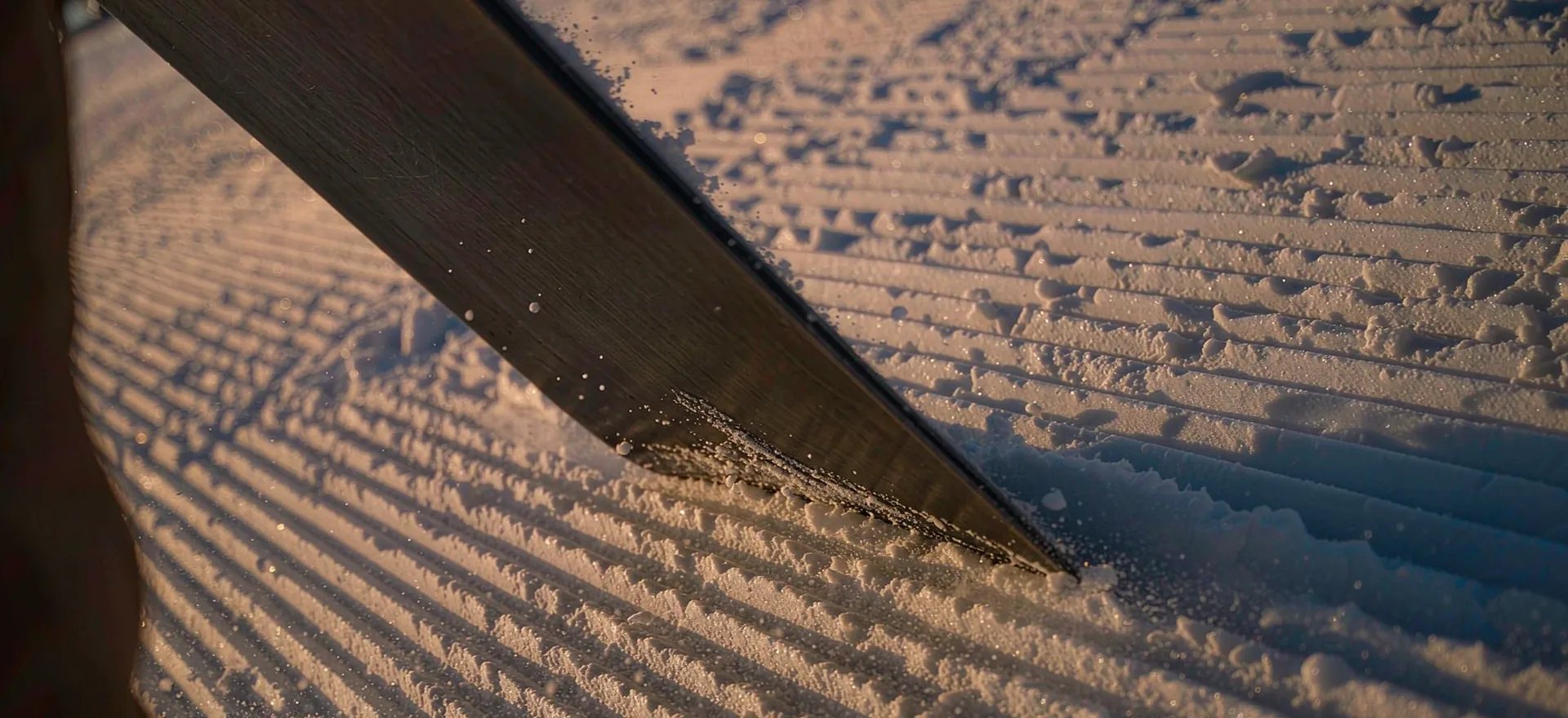 A close detail of a snowboard edge cutting into fresh groomed snow
