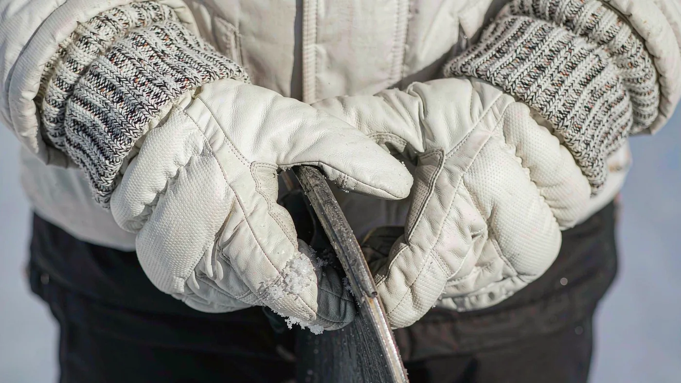 Gloved hands gripping the edge of a snowboard on a cold, overcast day