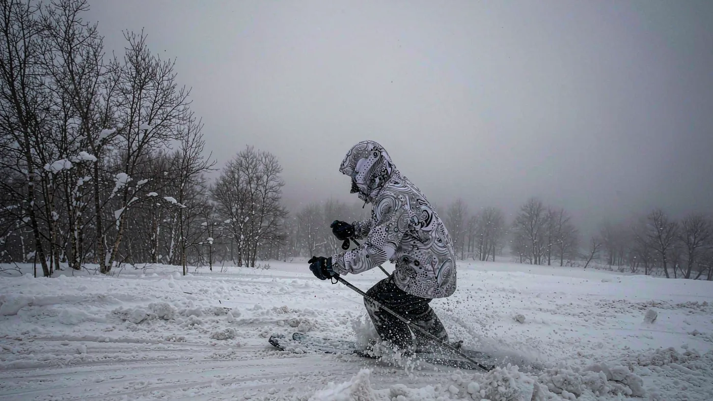 A rider in a hooded snowboard jacket on a wet, low-cloud Scottish piste