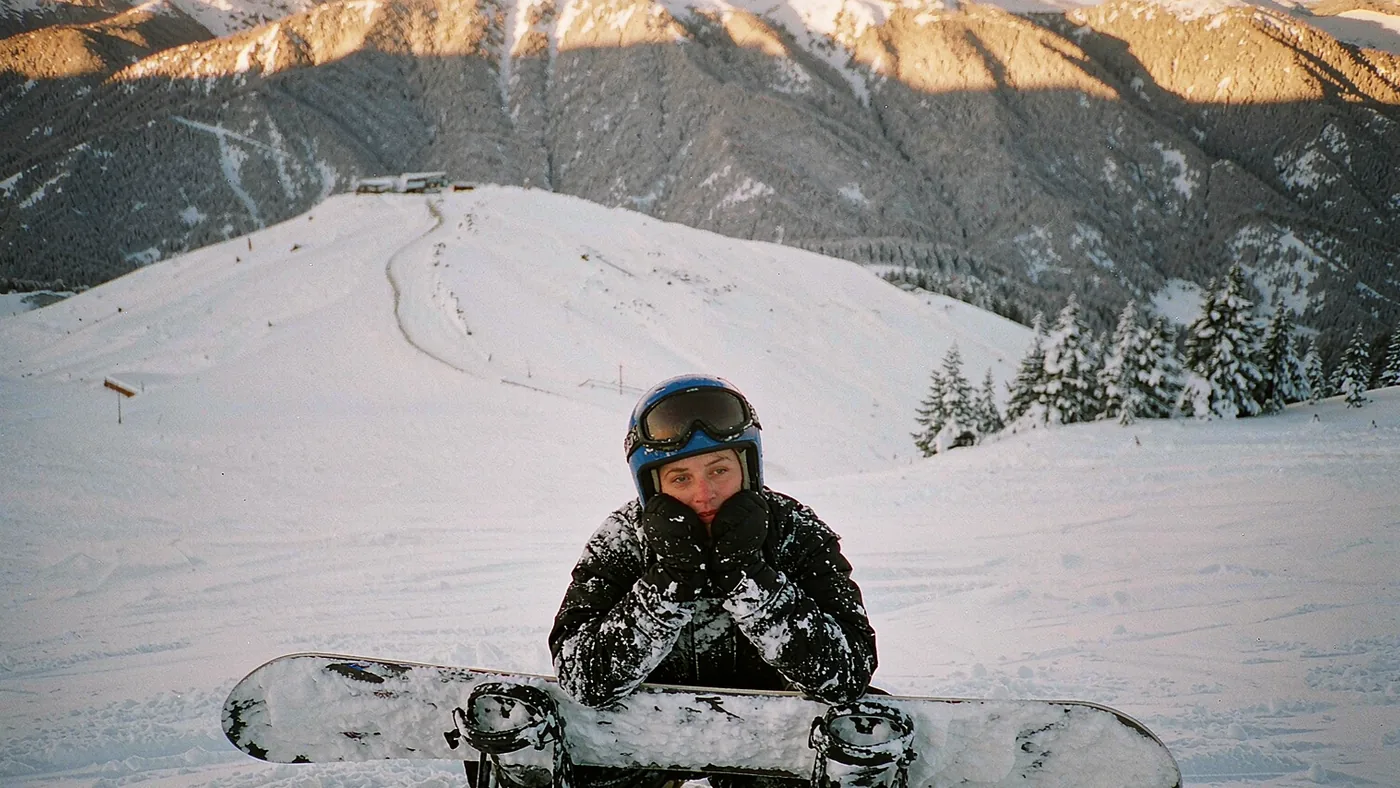 A beginner snowboarder sitting in the snow on a nursery slope with an instructor crouching beside them