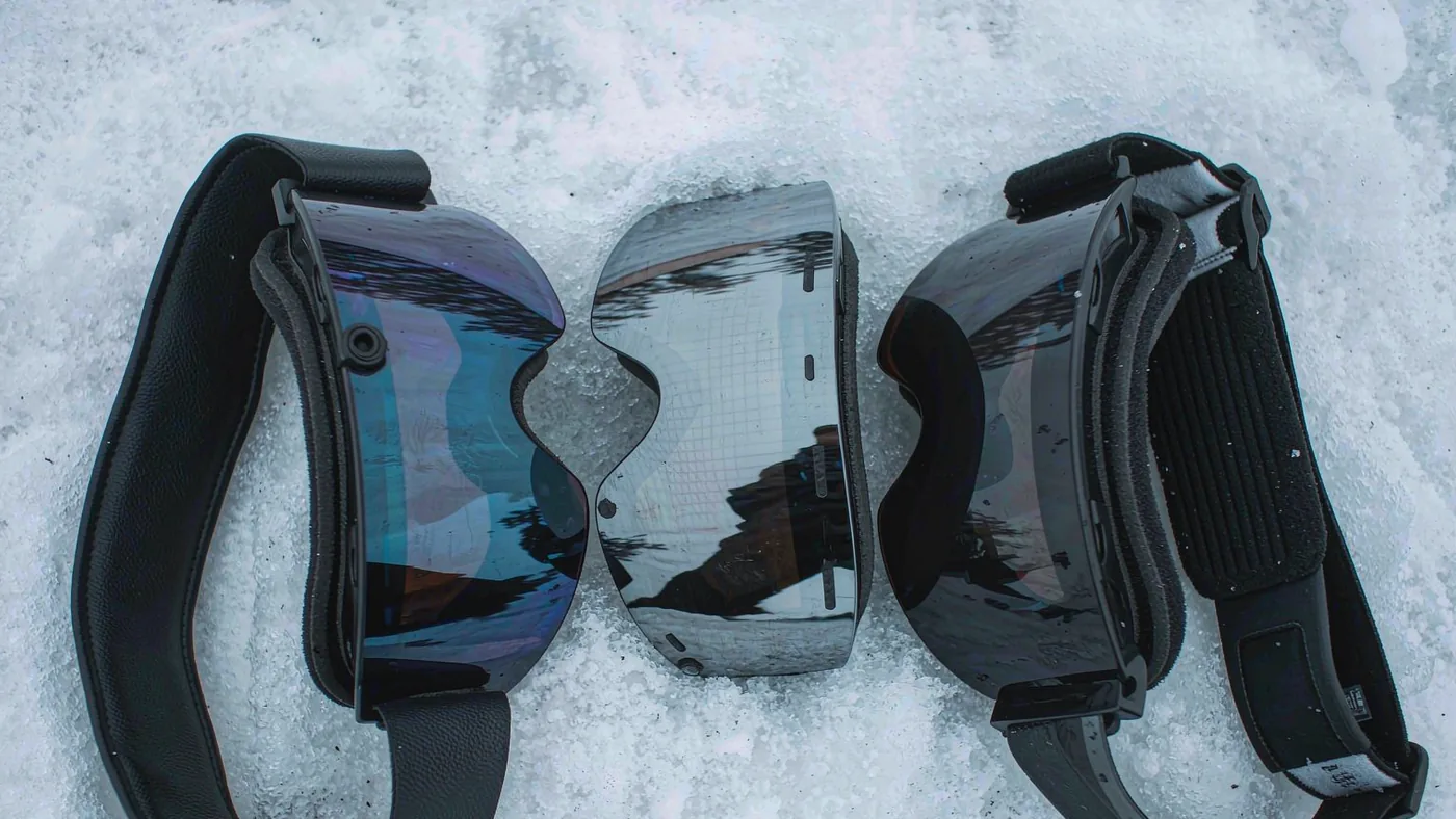 Three goggle lenses of different tint and mirror finish laid out side by side on snow
