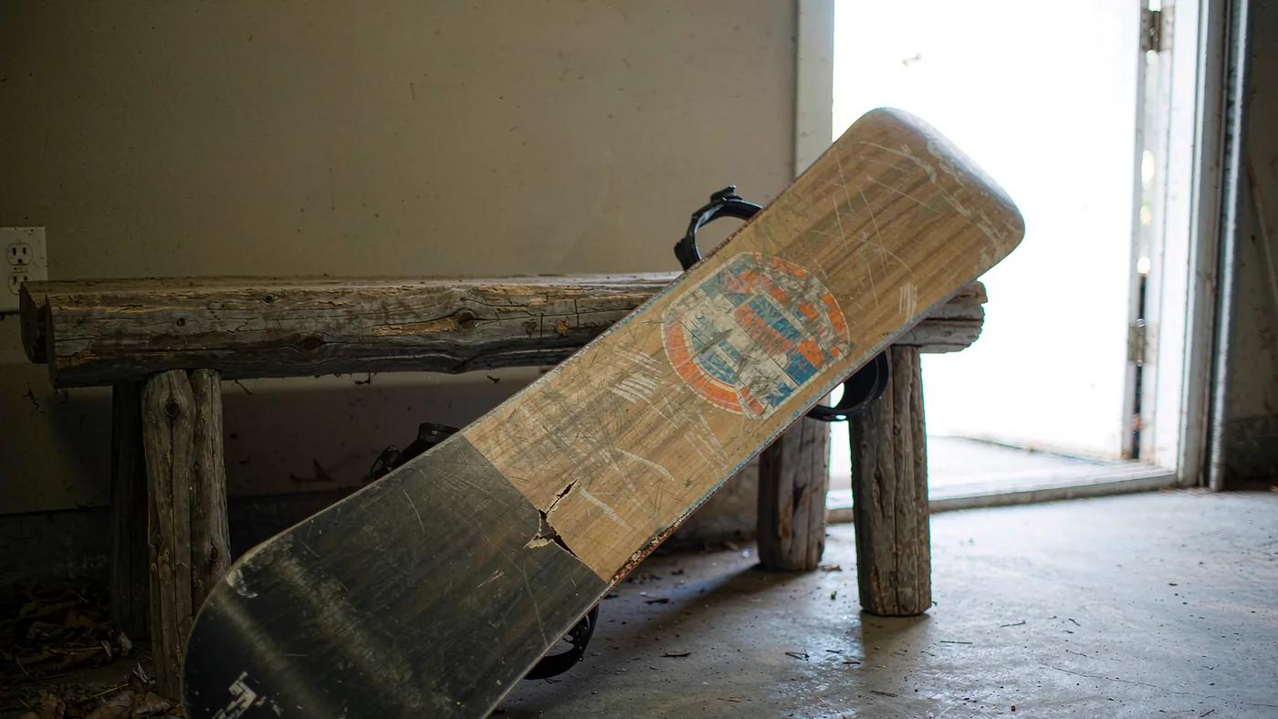 A used snowboard lying base-up on a workshop bench beside a scraper and a straight edge