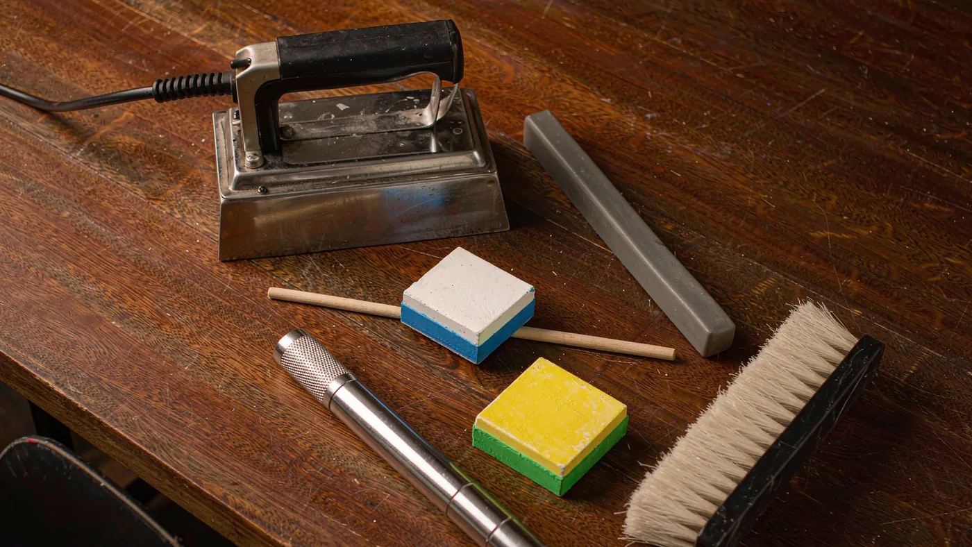 Hands running a waxing iron along the base of a snowboard supported on a workbench