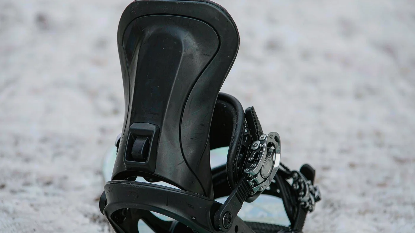 Close detail of a snowboard binding's highback, ankle strap and ratchet on a board on snow